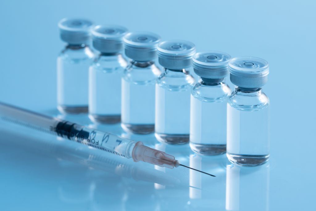 Vaccine vials with a syringe on a reflective surface