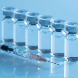 Vaccine vials with a syringe on a reflective surface
