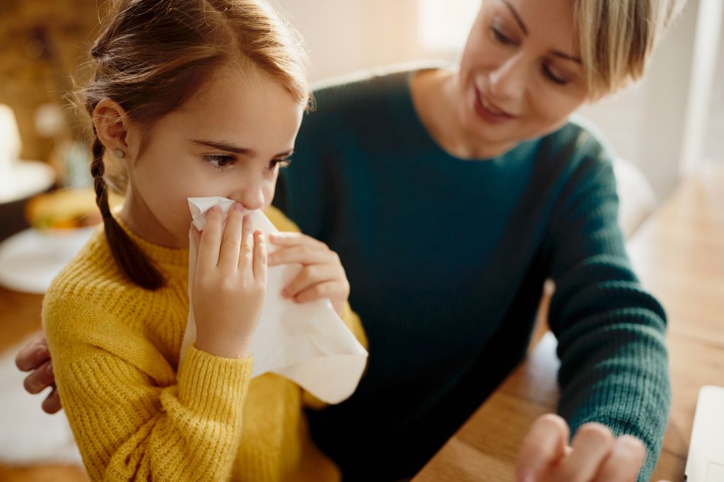 A child holding a tissue while being comforted by an adult at a table, suggesting they may not be feeling well.