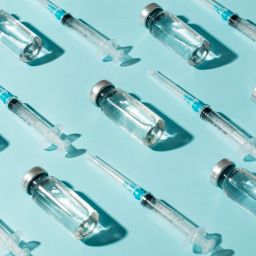 Glass vaccine vials and syringes arranged on a blue background, representing immunization and preventive healthcare.