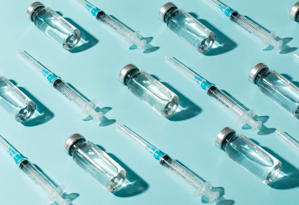 Glass vaccine vials and syringes arranged on a blue background, representing immunization and preventive healthcare.